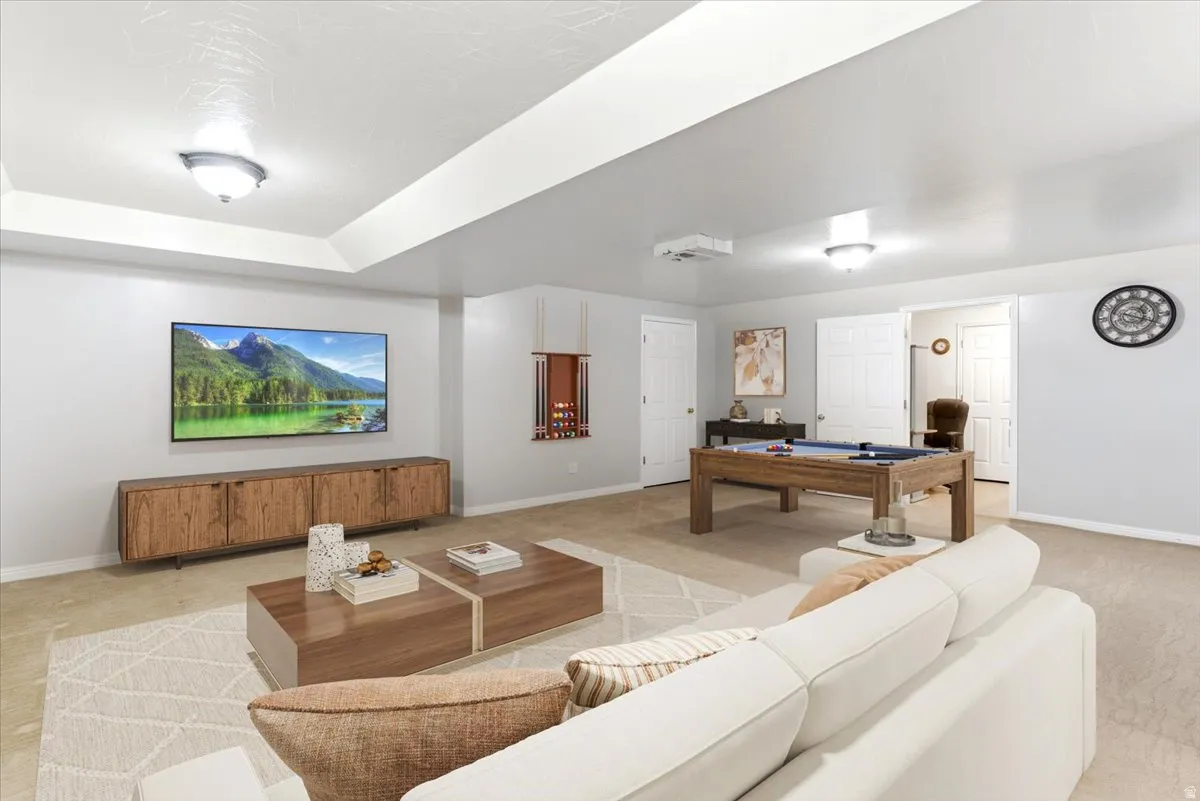 Spacious entertainment area featuring tray ceilings with flush-mount lighting, recessed projector, and a wood-finish media console