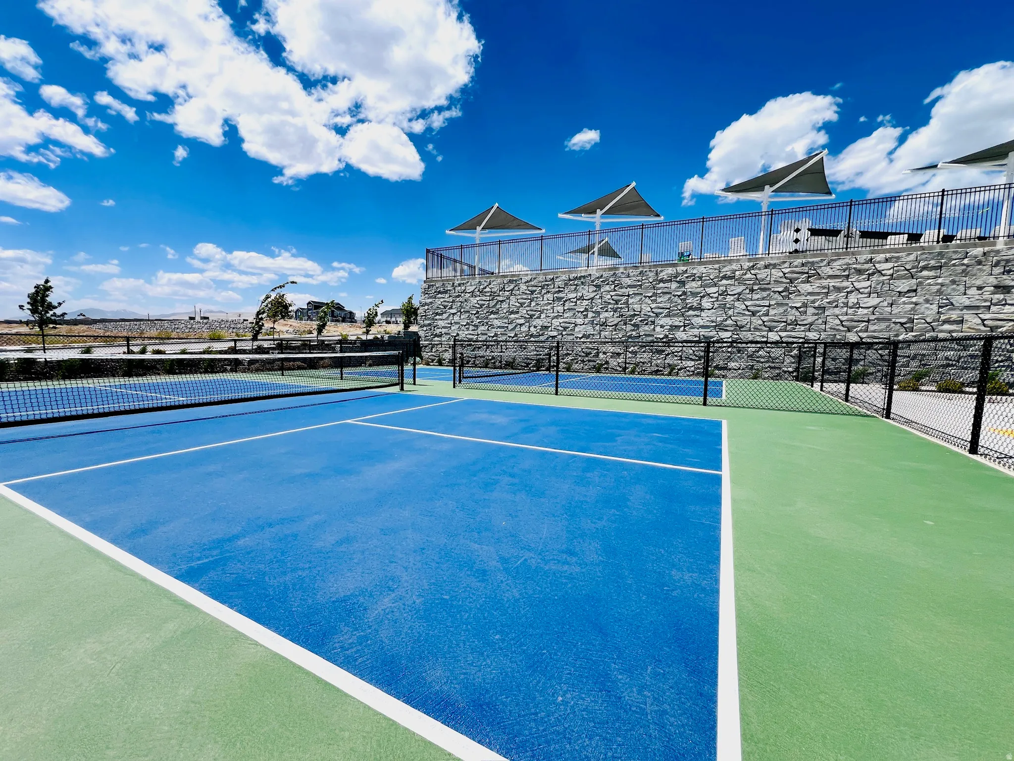 Recreational court area featuring two blue and green playing surfaces, black perimeter fencing, and a retaining wall with stone finish