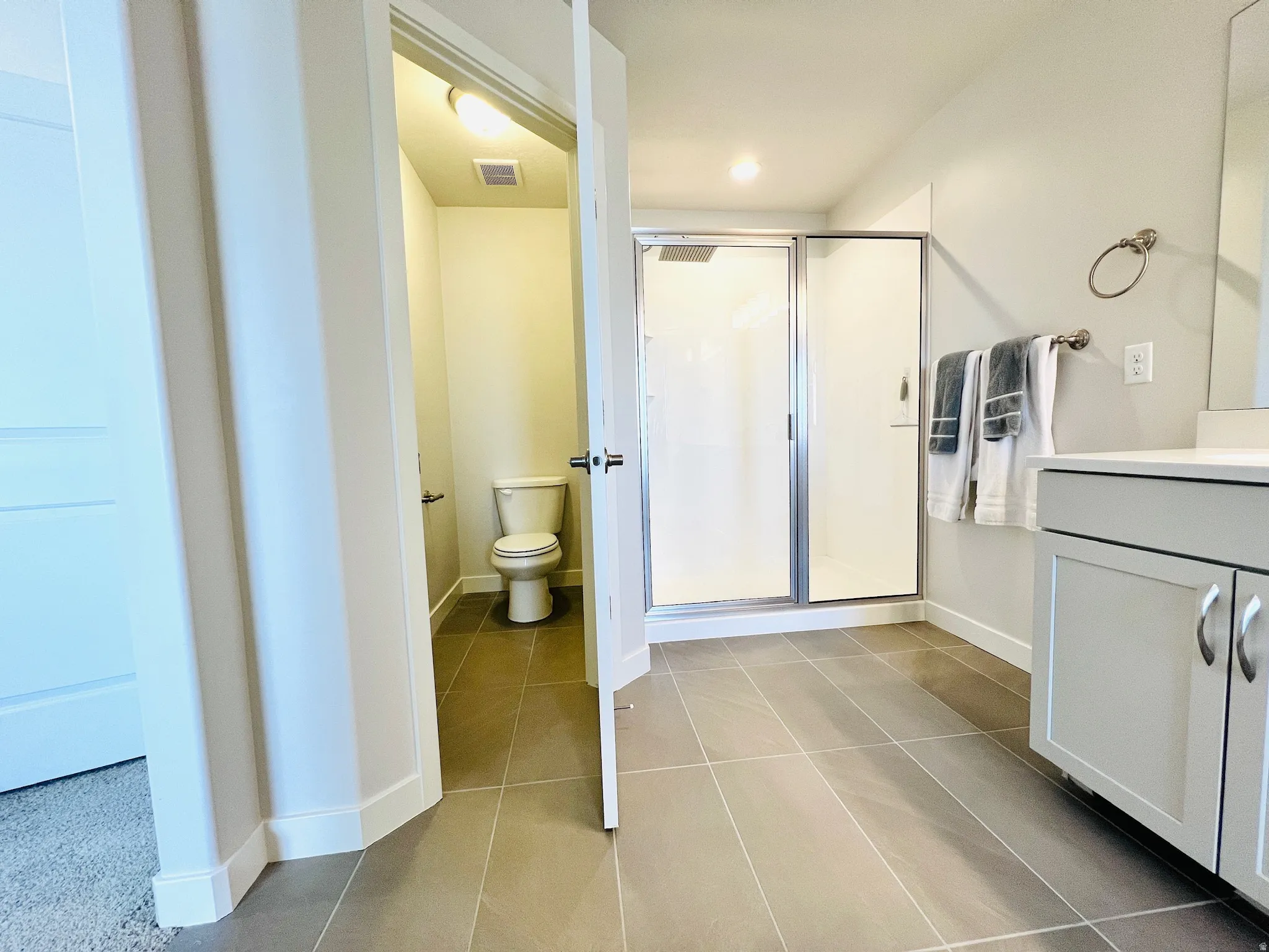 Spacious bathroom featuring large format floor tiles, a glass-enclosed shower, and a vanity with a light-colored countertop