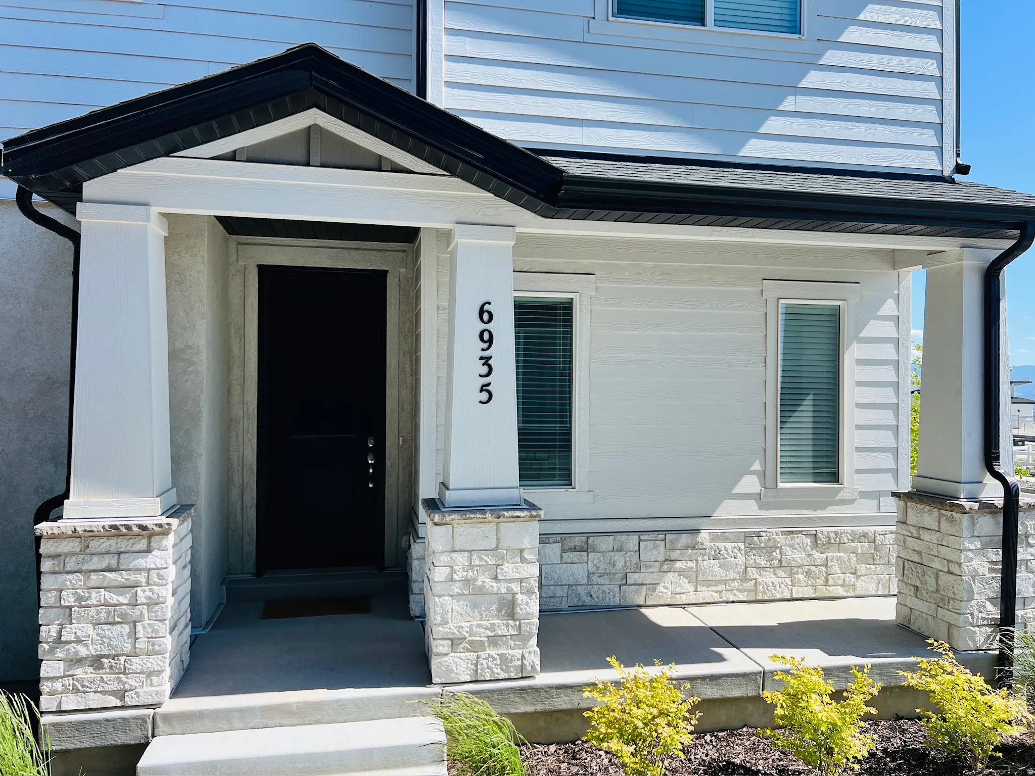 Front entry with a dark paneled door, stone facade accents, and white siding