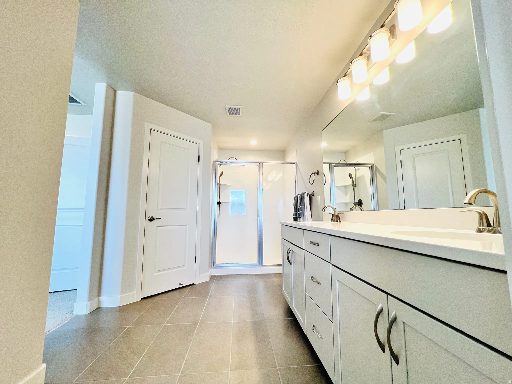 Contemporary bathroom featuring a double vanity with white cabinetry, a large frameless mirror, and a glass-enclosed shower