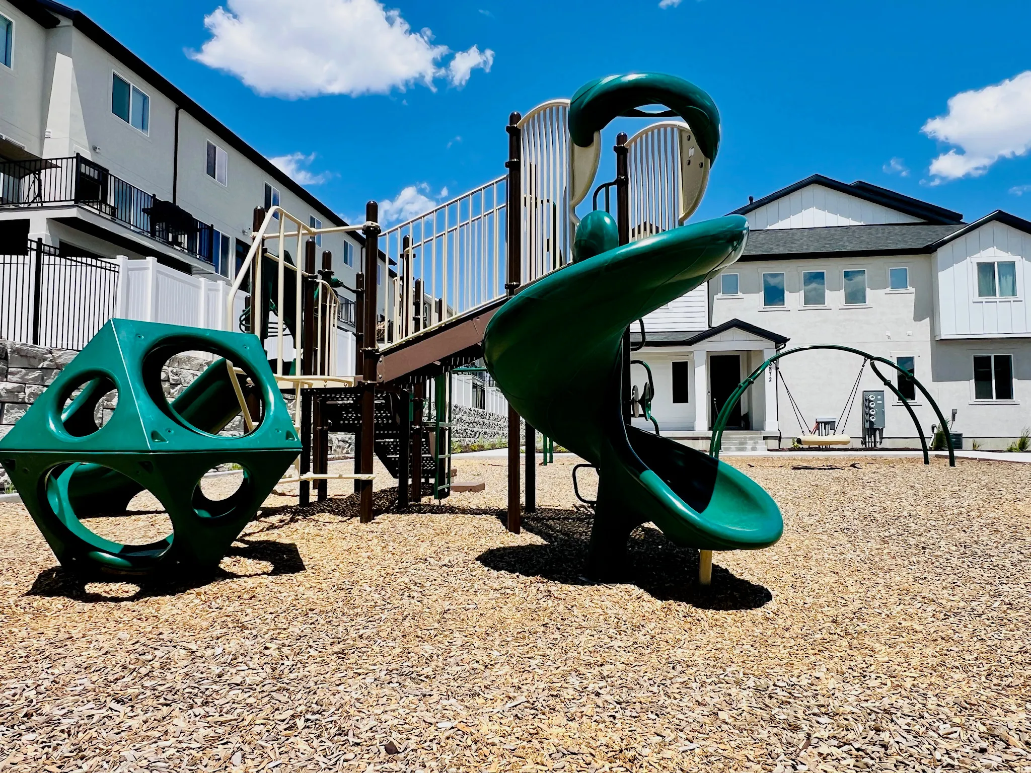 Community playground featuring green slide, climbing structure, and wood chip surfacing