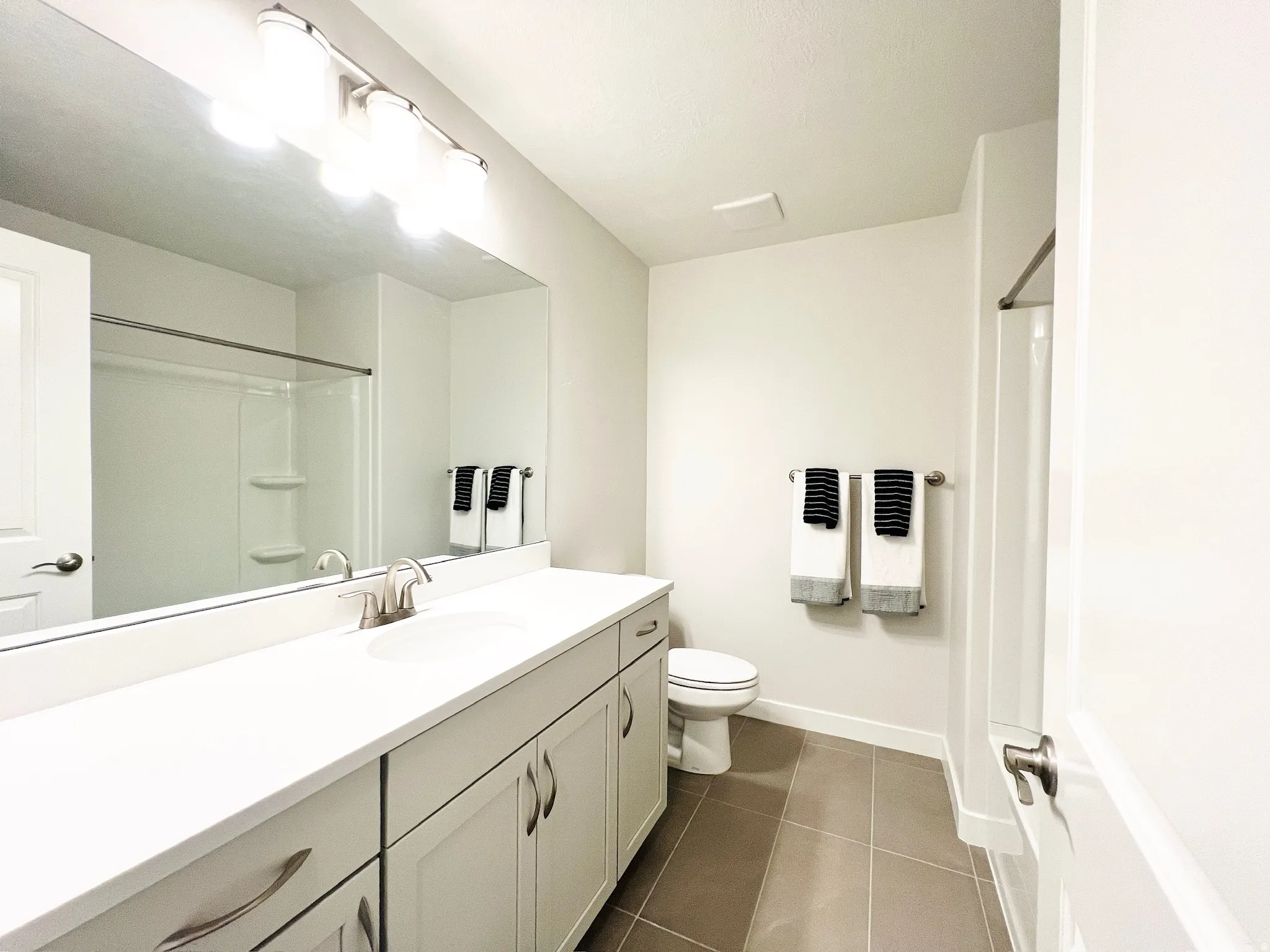 Bathroom featuring an extended single vanity with white cabinetry, a built-in shower and tub combination, a full-width mirror, and neutral-toned tile flooring
