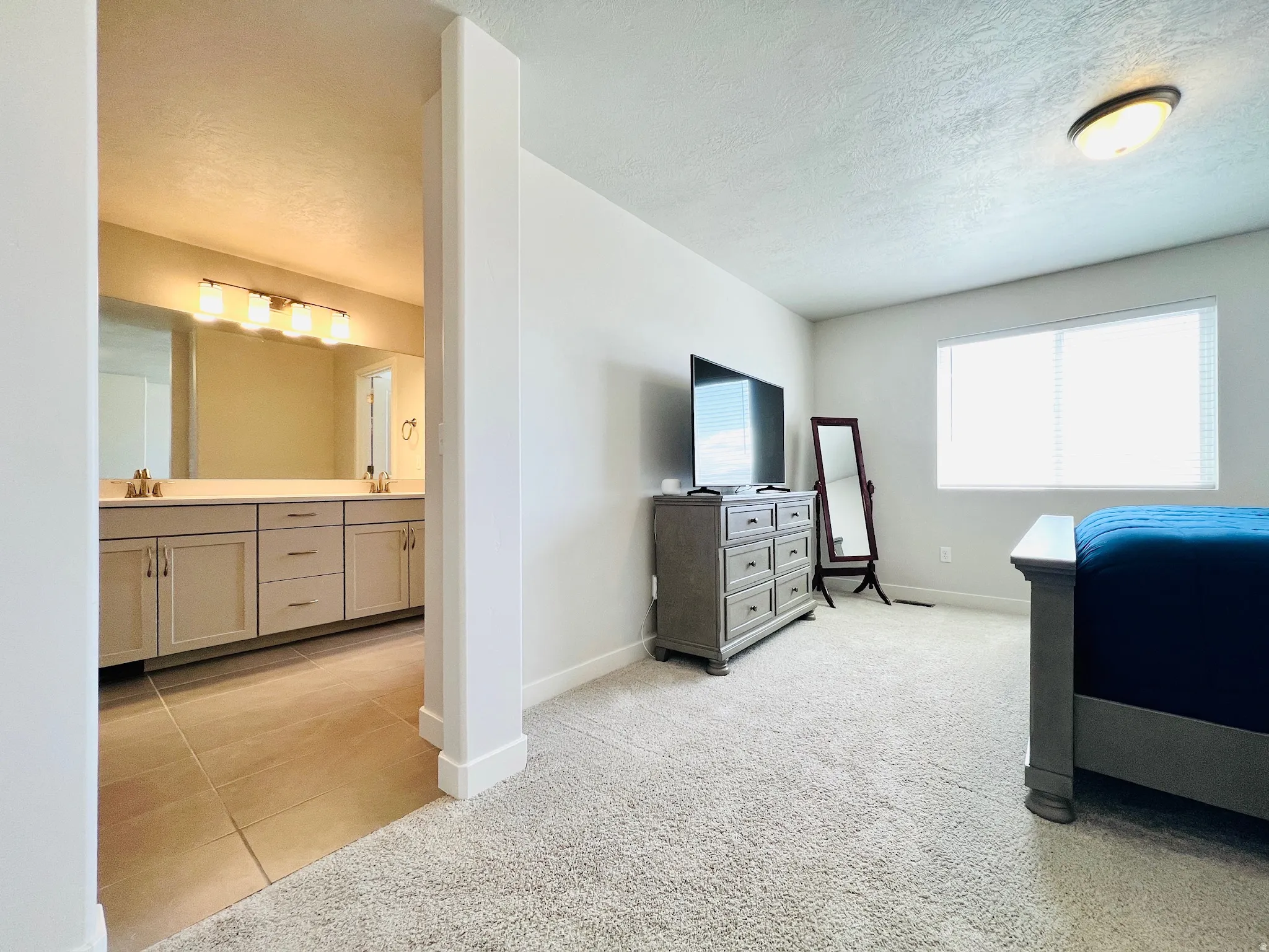 Bedroom featuring light-toned walls, a large window with blinds, and neutral carpeting