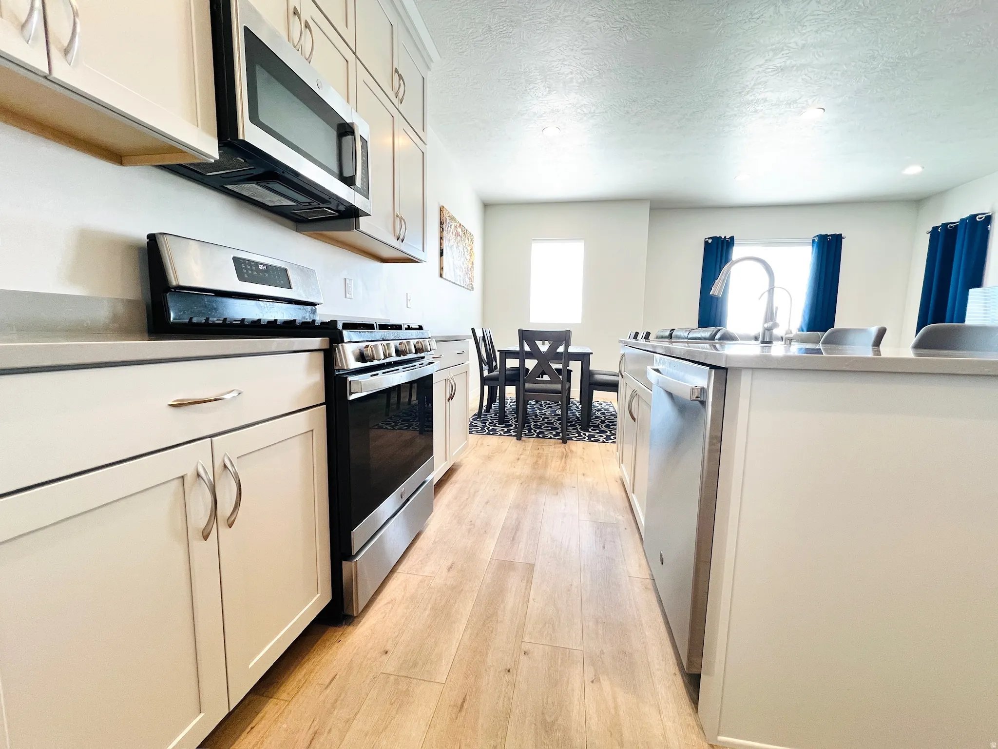 Kitchen featuring light-toned cabinetry with curved hardware, stainless steel appliances, a built-in microwave, and wood-finish flooring
