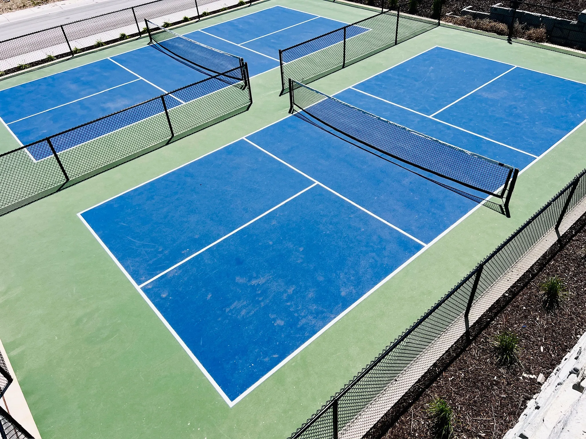 Two dedicated pickleball courts featuring blue playing surfaces with white line markings, surrounded by green perimeters