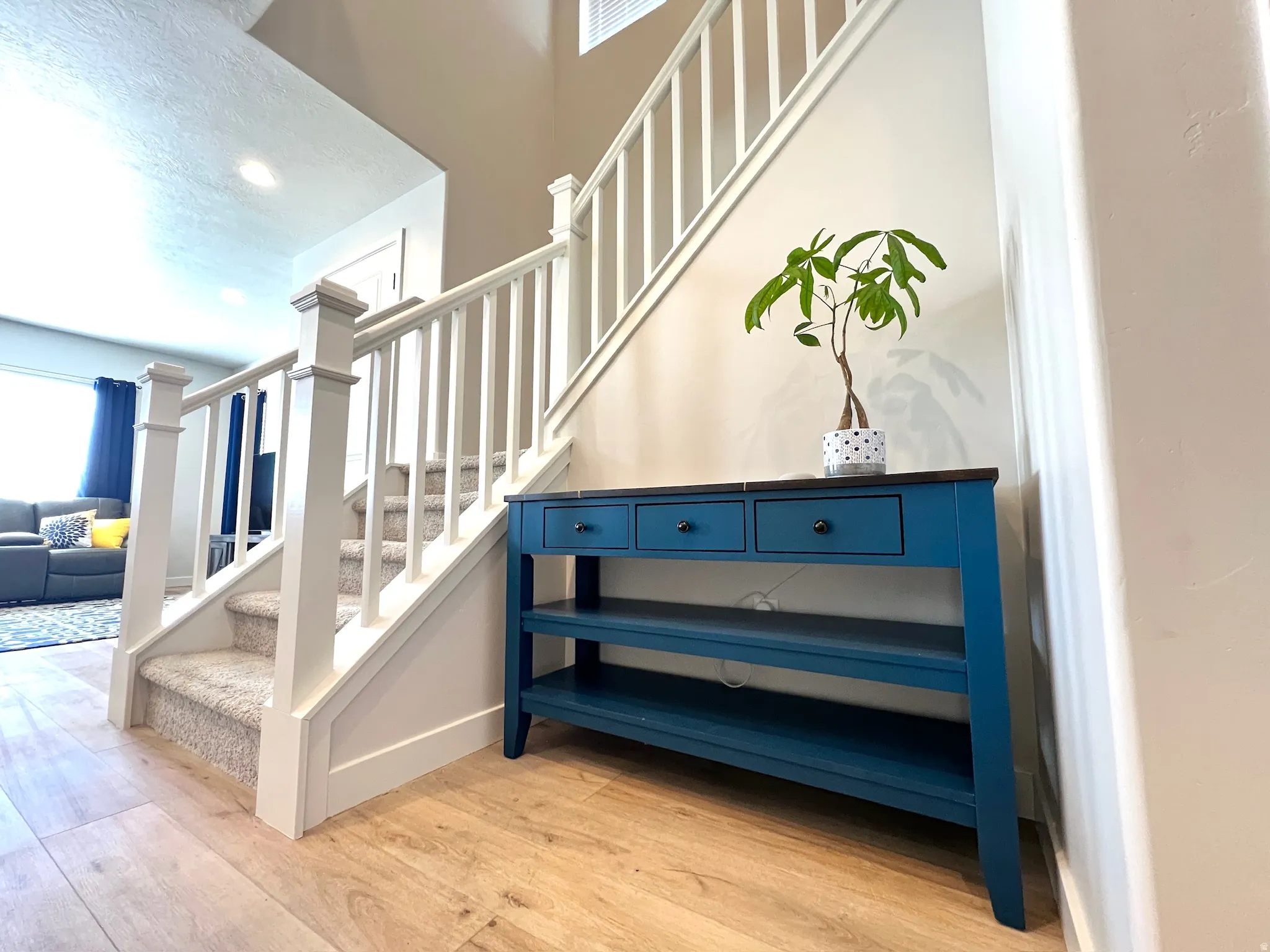 Entryway featuring wood-finish flooring, a carpeted staircase with white balusters, and a high ceiling