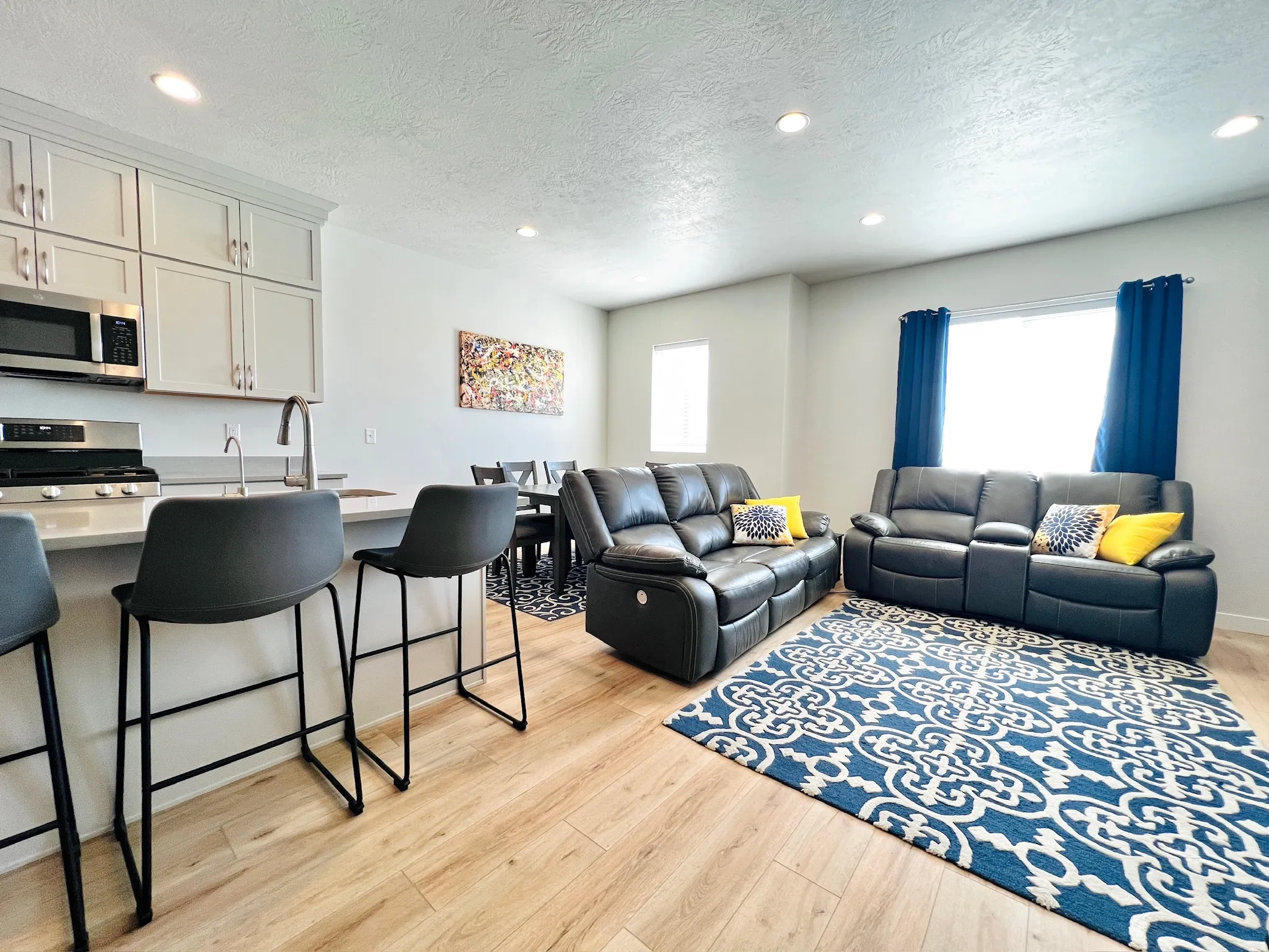 Open-concept living space featuring wood-finish flooring, recessed lighting, a kitchen island with seating, stainless steel appliances, and light-colored cabinetry