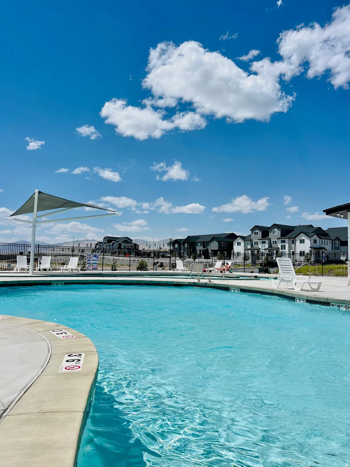Outdoor swimming pool with concrete decking, a white shade structure, and lounge chairs