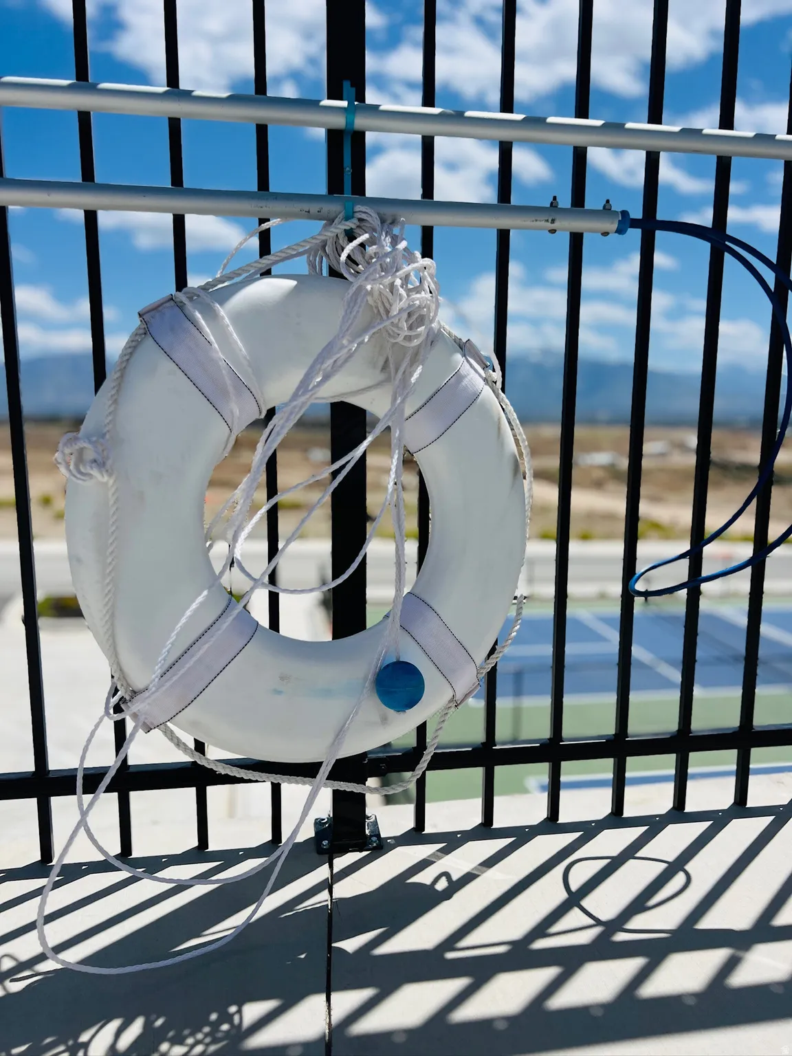 White life preserver hanging on a black metal fence with a tennis court visible in the background
