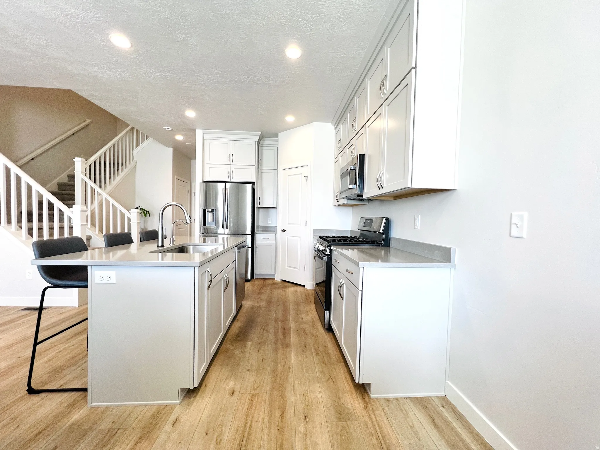 Open-concept kitchen featuring light-finish cabinetry, stainless steel appliances, a center island with a sink, and wood-finish flooring
