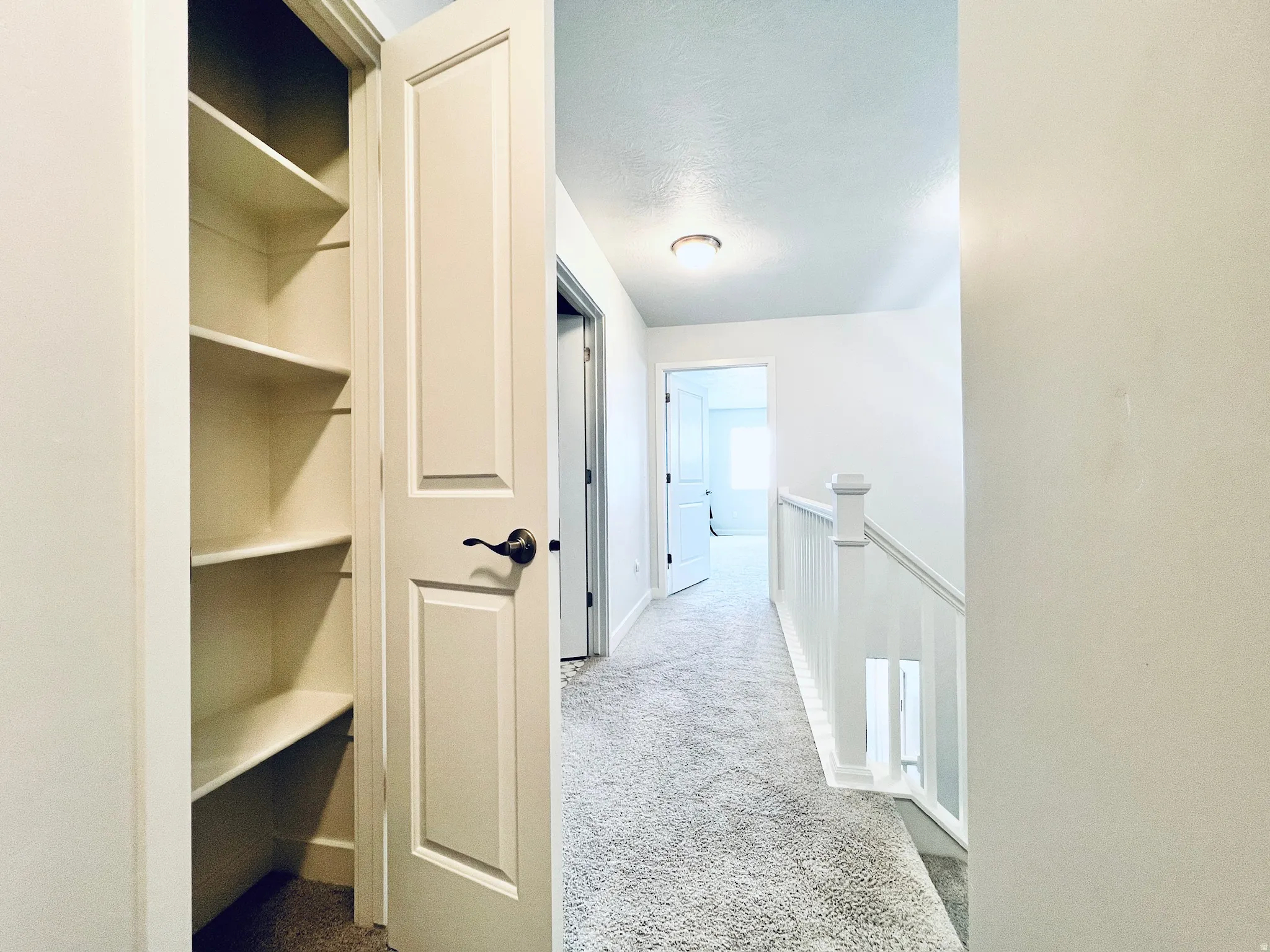 Hallway featuring a built-in shelving unit, paneled doors, light grey carpeting, white balustrade, and recessed lighting