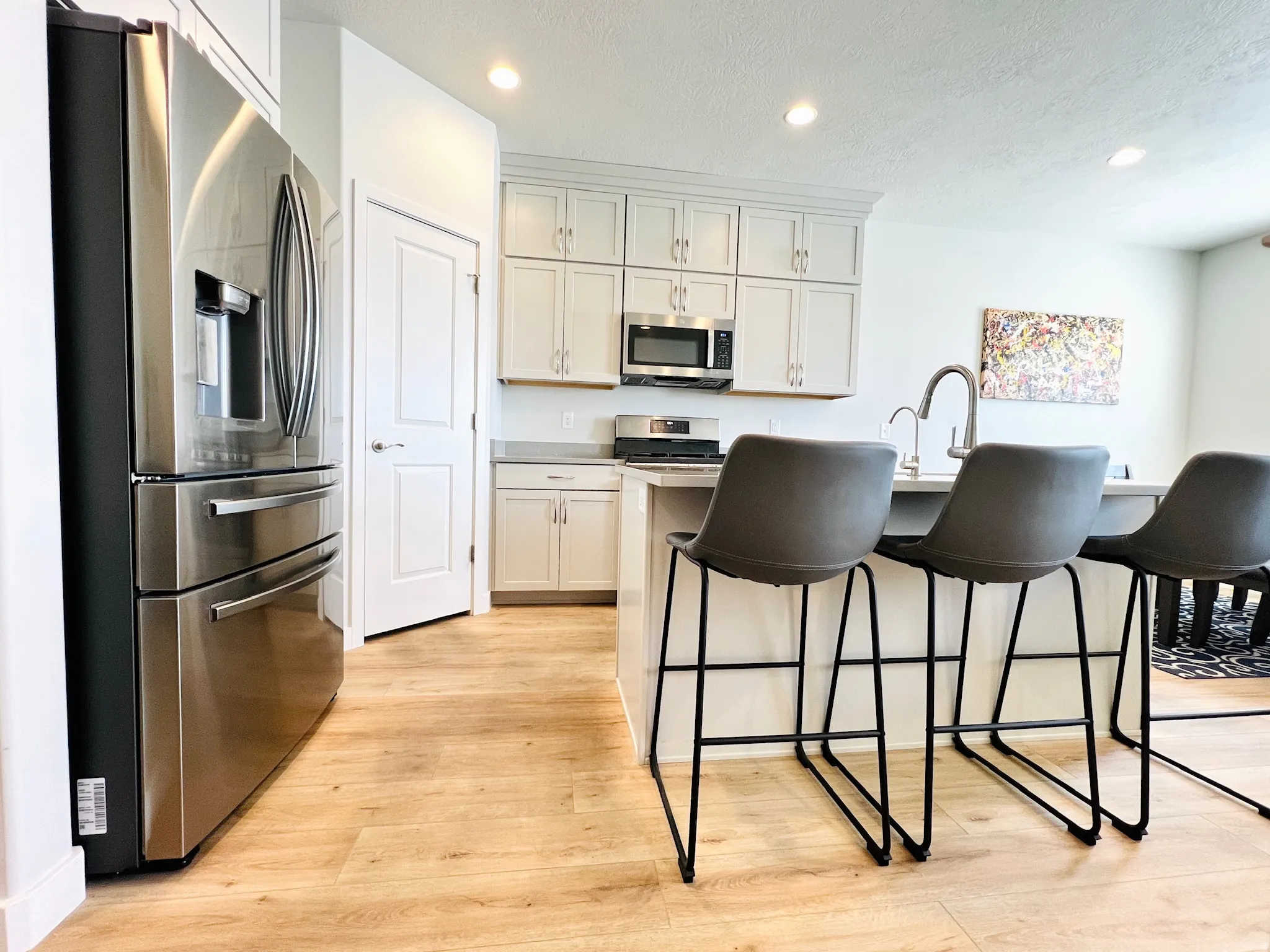 Kitchen featuring light wood-finish flooring, light grey cabinetry, stainless steel appliances, and an island with a stainless steel faucet