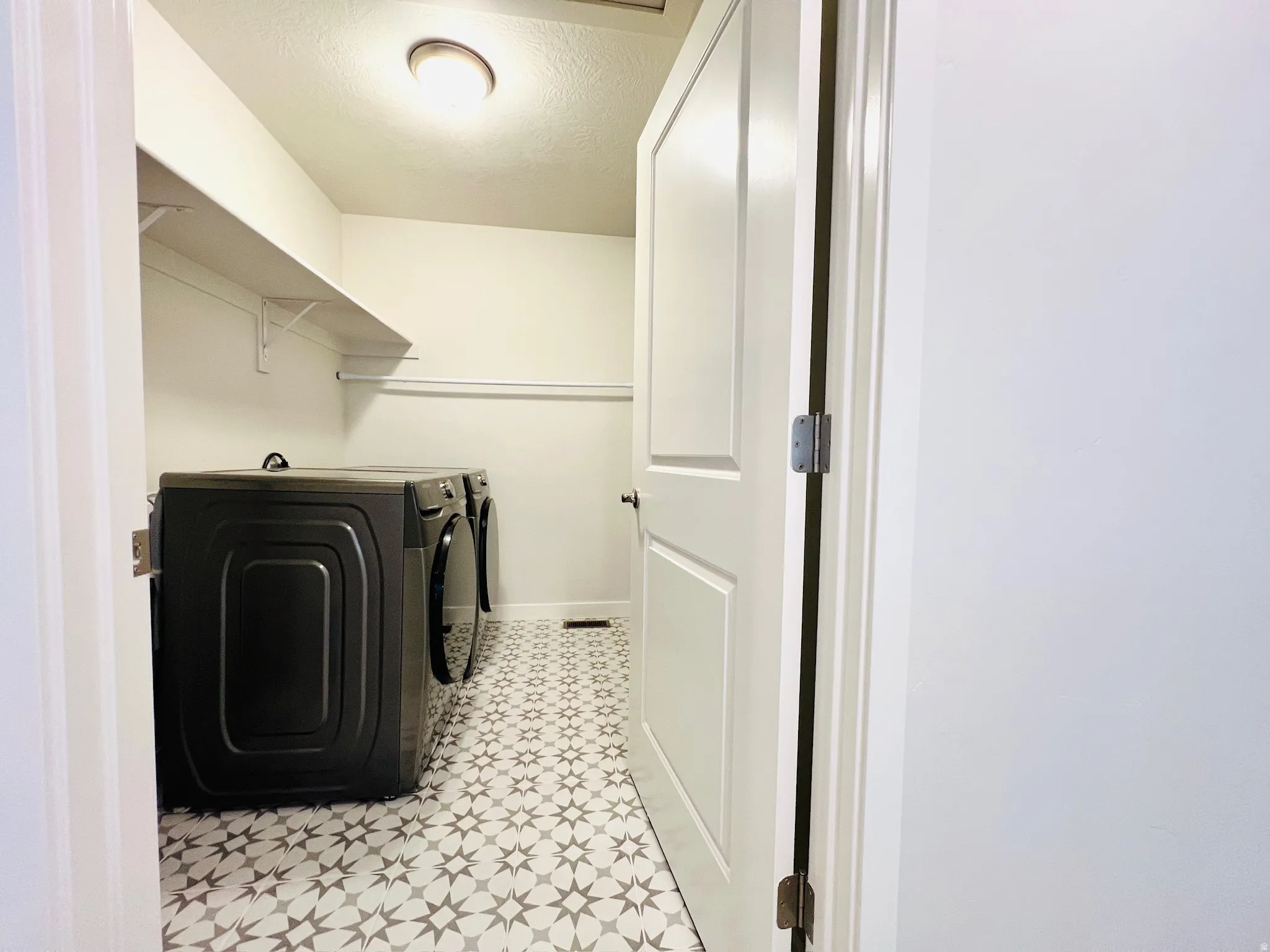 Laundry area featuring patterned floor tiles and an overhead light fixture