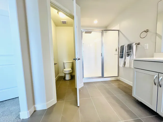 Spacious bathroom featuring large format floor tiles, a glass-enclosed shower, and a vanity with a light-colored countertop