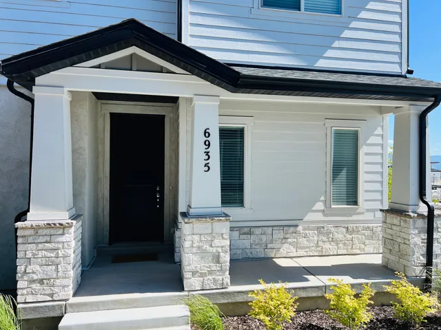 Front entry with a dark paneled door, stone facade accents, and white siding
