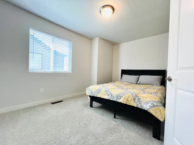 Bedroom featuring light-toned carpeting, a window with blinds, and white walls