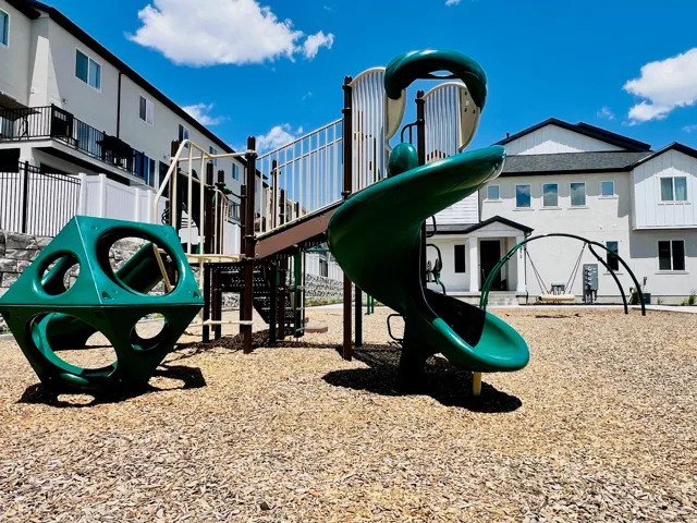Community playground featuring green slide, climbing structure, and wood chip surfacing