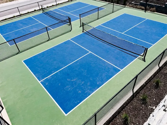 Two dedicated pickleball courts featuring blue playing surfaces with white line markings, surrounded by green perimeters