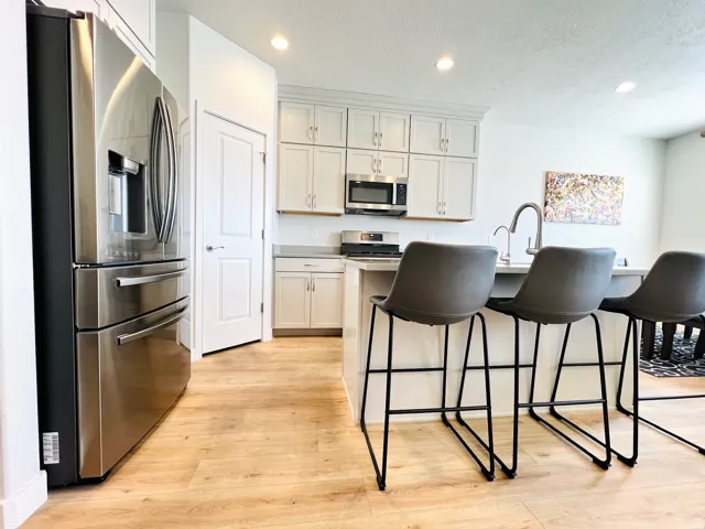 Kitchen featuring light wood-finish flooring, light grey cabinetry, stainless steel appliances, and an island with a stainless steel faucet