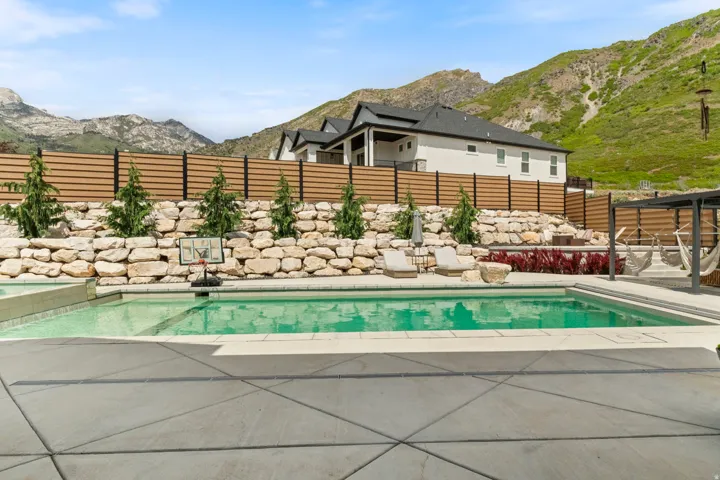 Outdoor swimming pool with integrated spa, surrounded by extensive concrete patio and a stone retaining wall