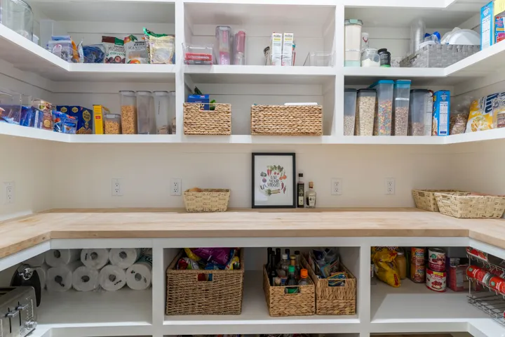 Dedicated pantry featuring extensive open shelving, wrap-around wood-finish countertops, built-in lower storage compartments, and multiple electrical outlets