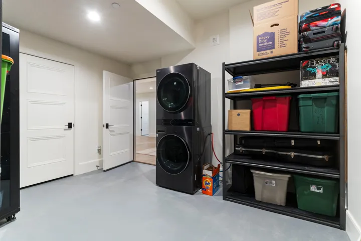Laundry area featuring a stacked washer and dryer unit, light gray flooring, recessed lighting, and white paneled doors with black hardware