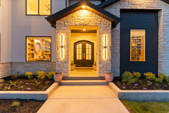 Stone and dark siding exterior with arched double entry doors, contemporary vertical sconces, a covered entryway, and concrete walkway