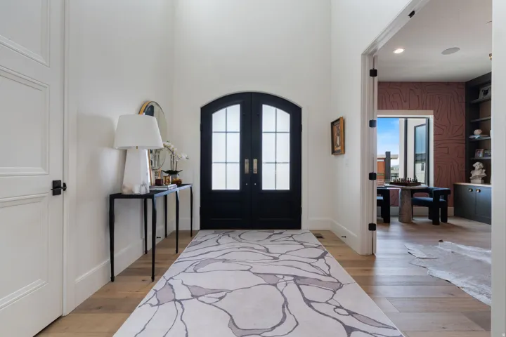 Grand entryway featuring an arched double door with glass panels, light wood-finish flooring, and high ceilings