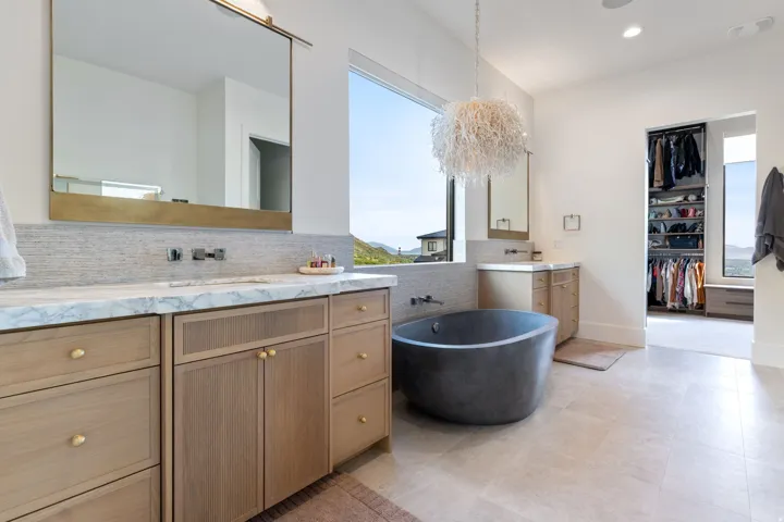 Contemporary bathroom featuring a freestanding soaking tub, dual vanity with light wood cabinetry, marble-finish countertop, and large format floor tiling