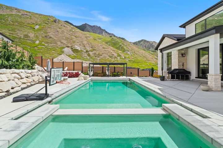 Expansive outdoor living area featuring a rectangular pool with an integrated spa, concrete patio, and stacked stone retaining wall