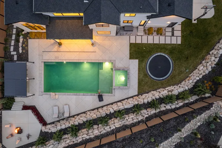 Expansive outdoor living area featuring a rectangular swimming pool with integrated spa, a paved patio, and a dedicated fire pit area