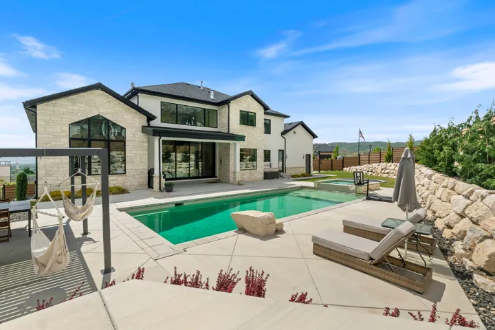 Expansive outdoor living area featuring a rectangular swimming pool with a connected hot tub