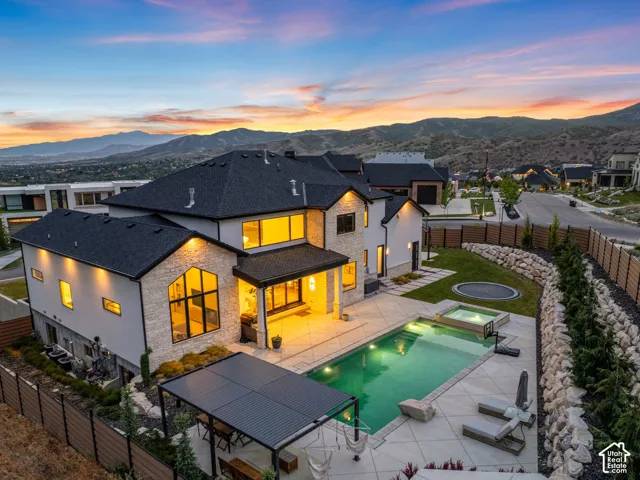 Contemporary residence featuring a dark shingle roof, light-colored stone and stucco exterior, an in-ground swimming pool, and a spa