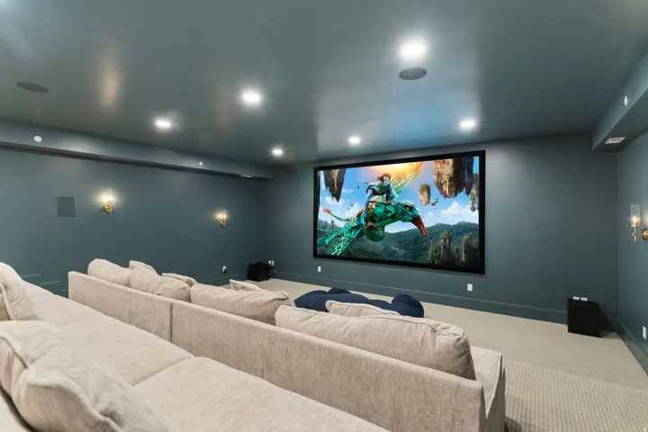 Dedicated media room featuring a large projection screen, recessed ceiling lighting, and wall-mounted sconces