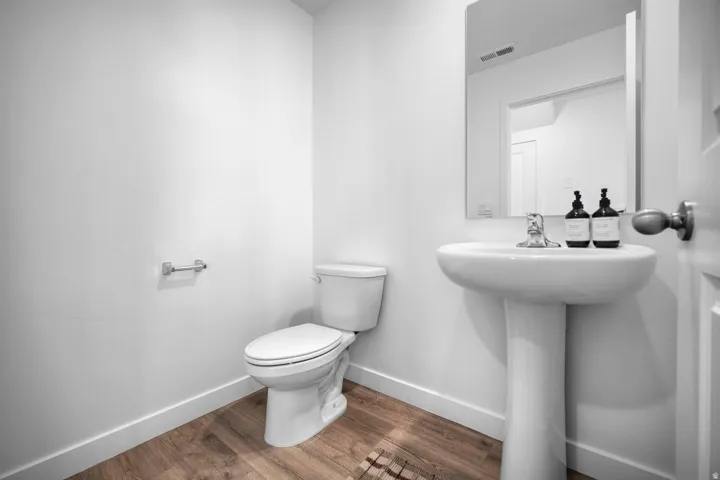 Pedestal sink with chrome faucet, wall-mounted mirror, and wood-finish flooring