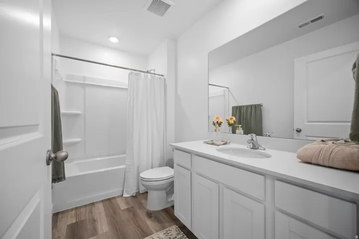 Bathroom featuring a white vanity with an integrated sink, a large wall-mounted mirror, and wood-finish flooring
