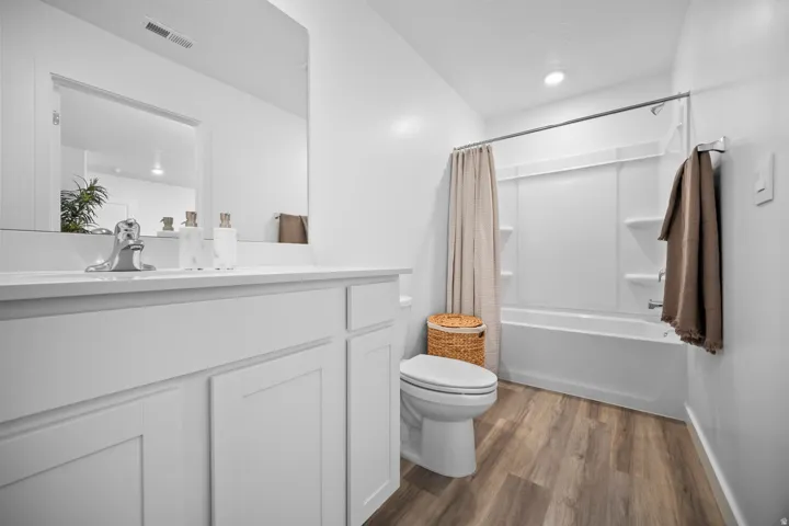 Bathroom featuring a single vanity with white cabinetry, a large mirror, a white bathtub with a shower, and wood-finish flooring