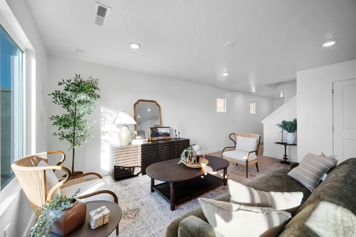 Bright living area featuring expansive windows, recessed lighting, white walls, wood-finish flooring, and a staircase with white balusters