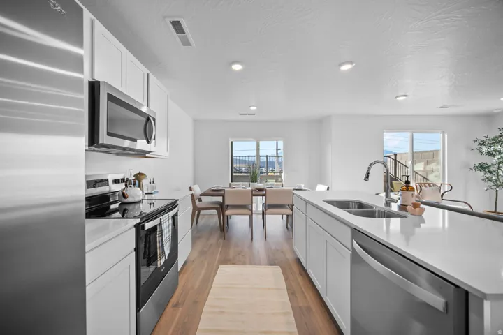 Open-concept kitchen featuring stainless steel appliances, light wood-finish flooring, white cabinetry, a kitchen island with an undermount sink, and recessed lighting