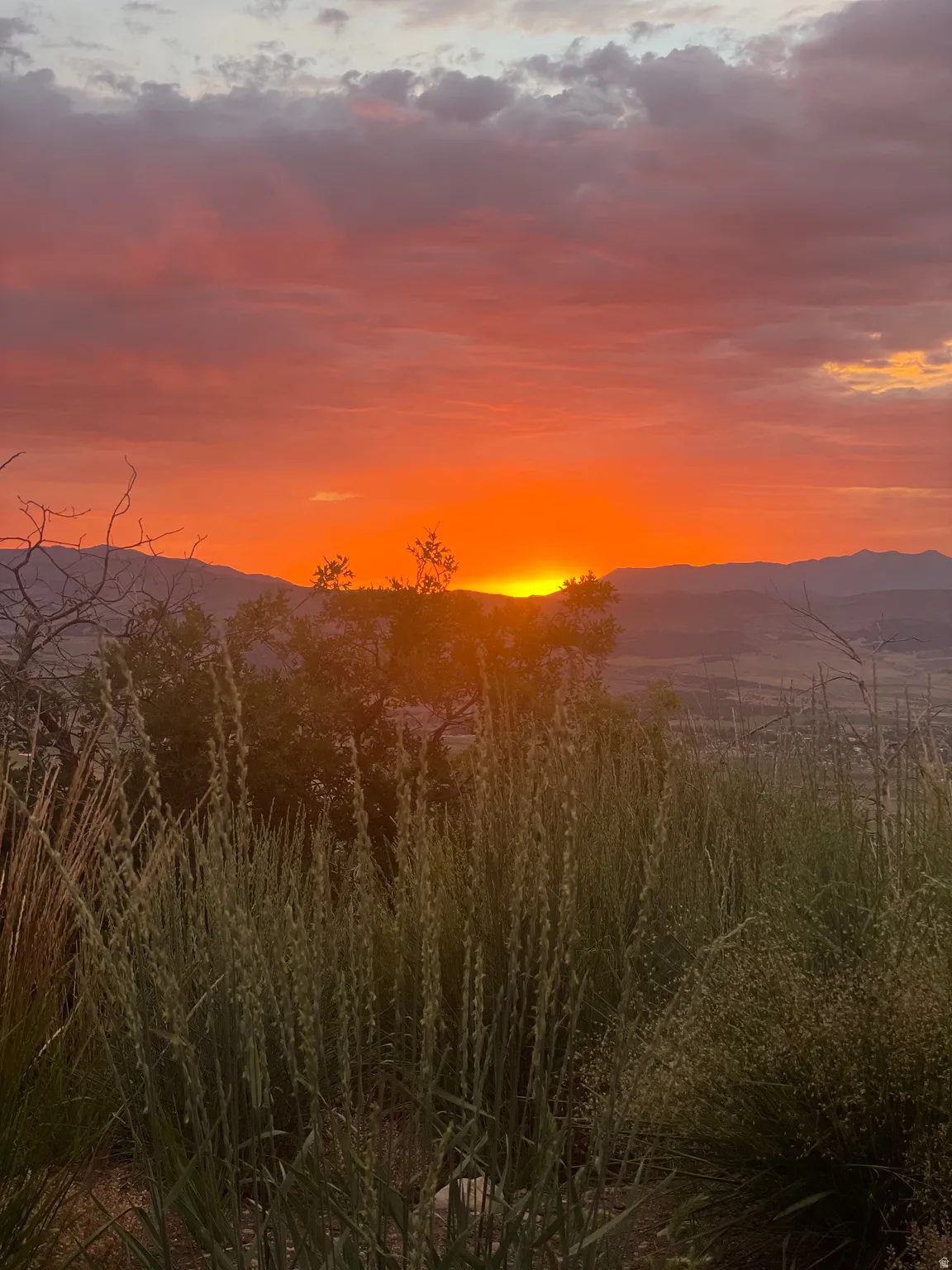 Expansive mountain range backdrop with a dramatic sunset, showcasing vibrant orange and red skies