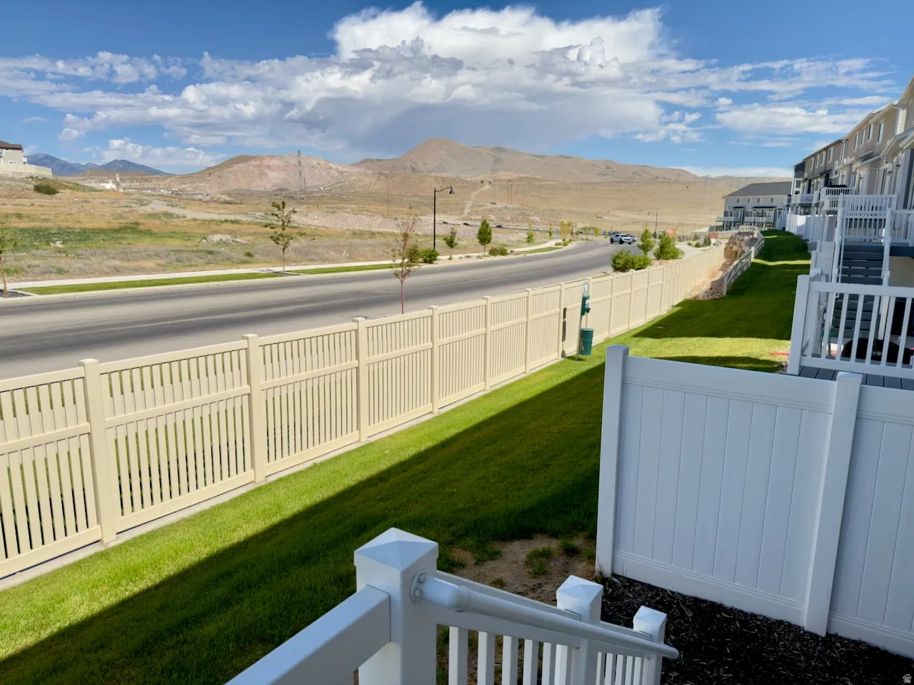 Fenced backyard area featuring a manicured lawn, white railings, and a cream-colored slat fence bordering the street