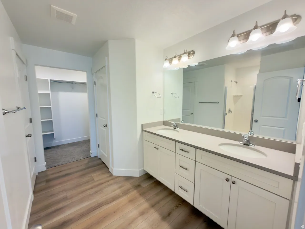 Bathroom featuring wood-finish flooring and a dual vanity with undermount sinks and light-toned countertops