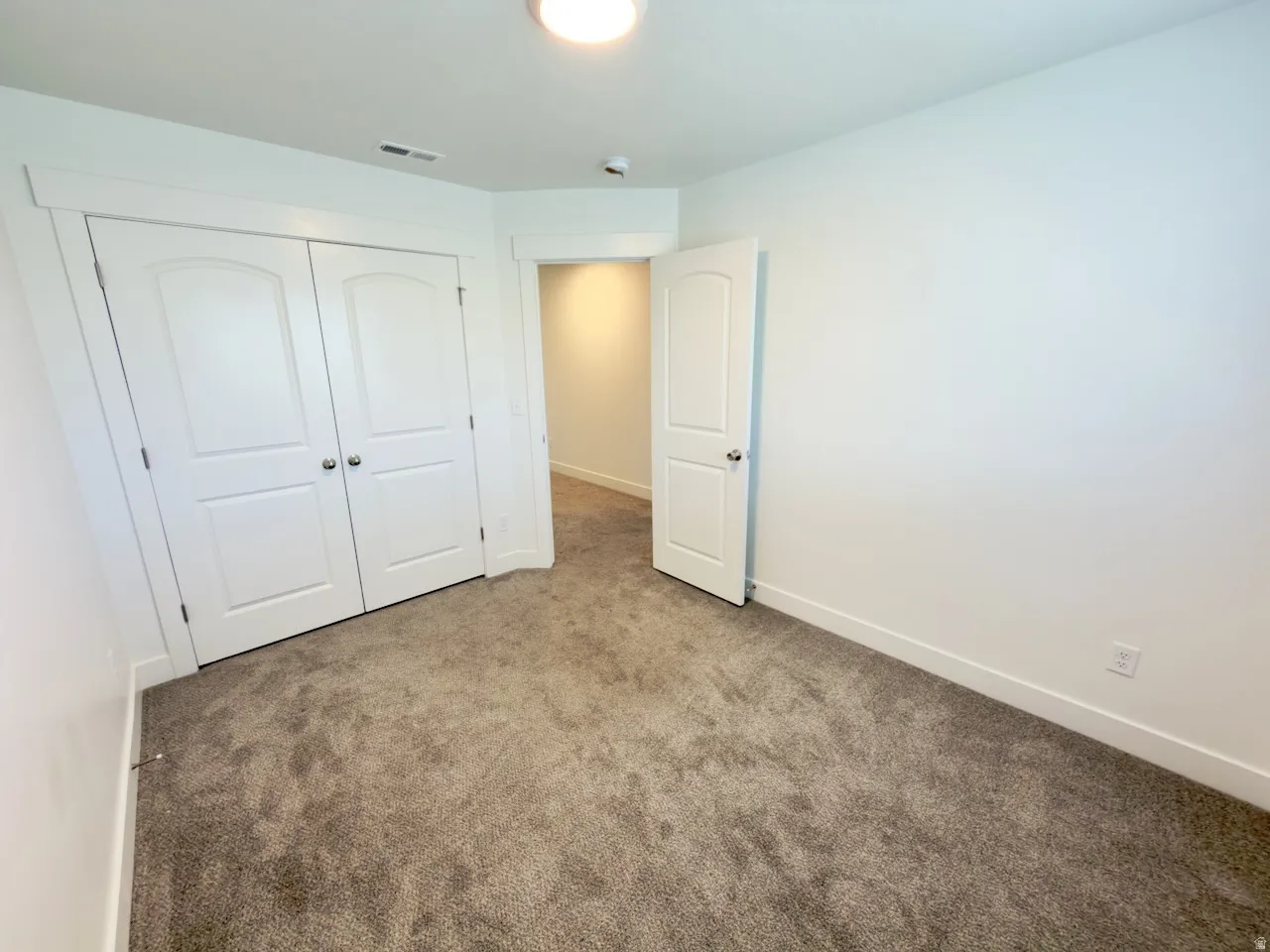 Neutral tone wall paint with white trim, gray carpet flooring, and a double-door closet with arched paneling