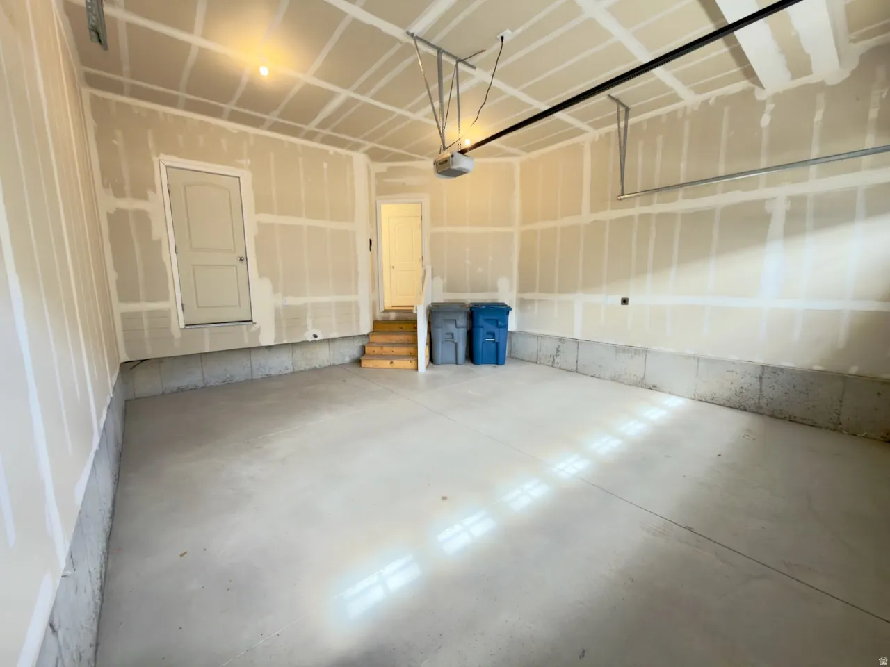 Spacious garage featuring a concrete floor, overhead lighting, garage door opener, and interior access door