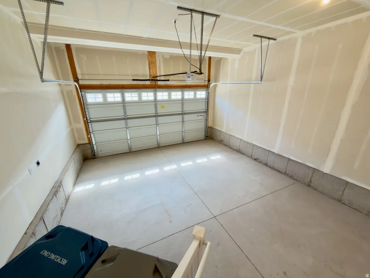 Spacious garage featuring a sectional overhead door with upper window inserts, concrete flooring, and an automatic garage door opener system