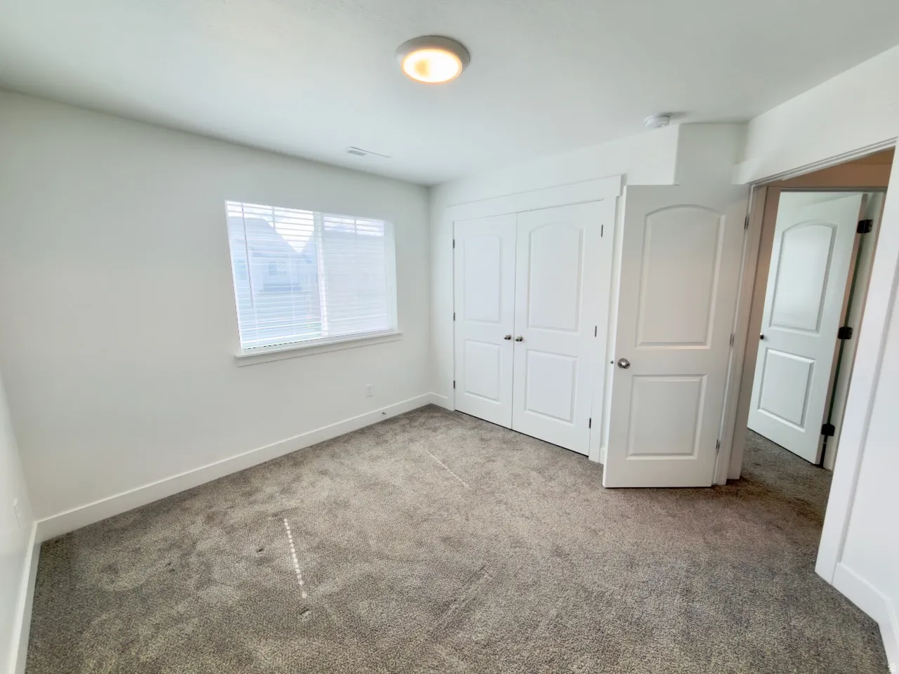 Carpeted interior room featuring white walls, a single window with blinds, and a flush-mount ceiling light