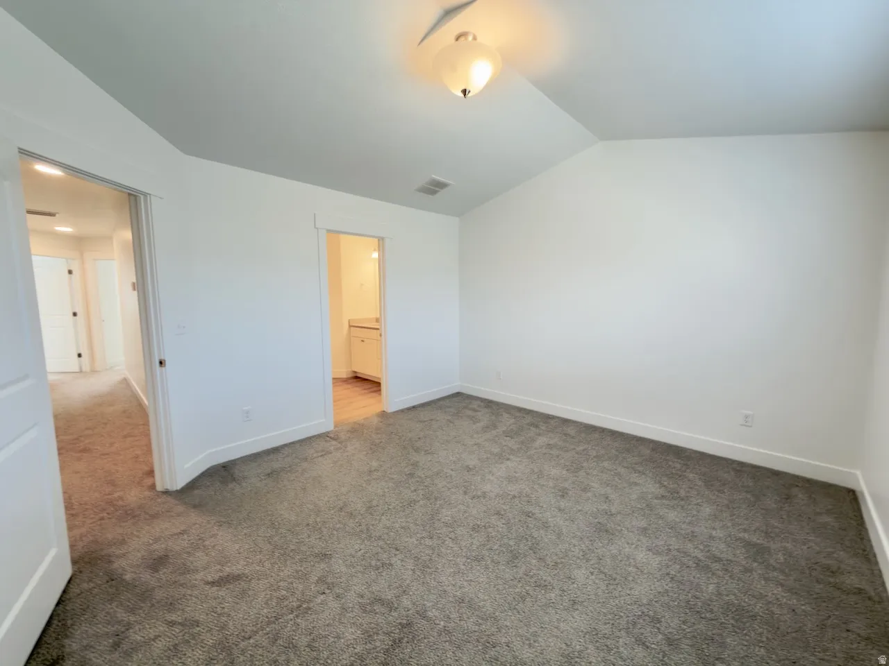 Spacious carpeted room with a vaulted ceiling and a semi-flush mount light fixture