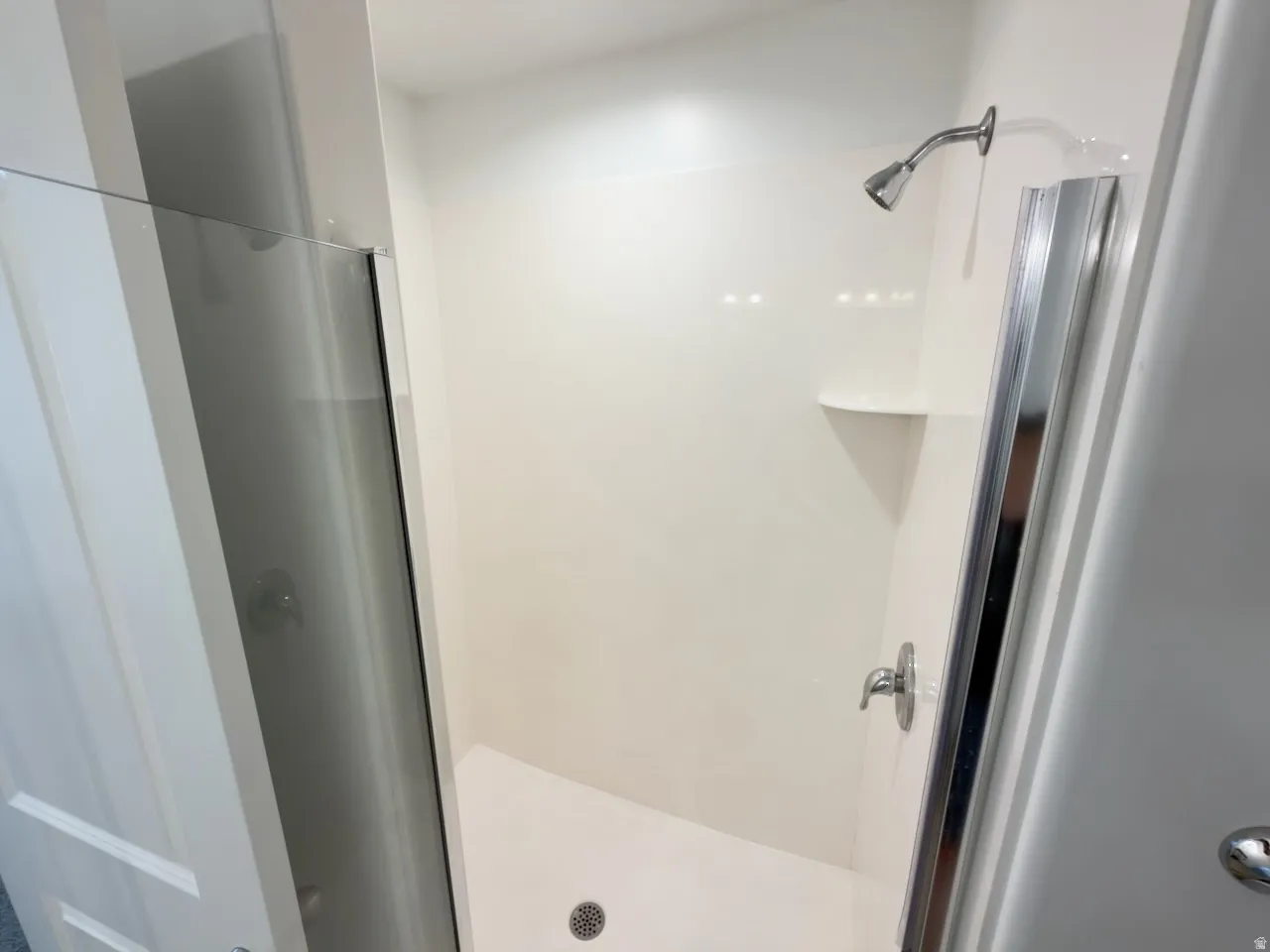 Shower enclosure featuring a chrome shower head and handle, integrated corner shelf, and a glass shower door with a polished chrome frame