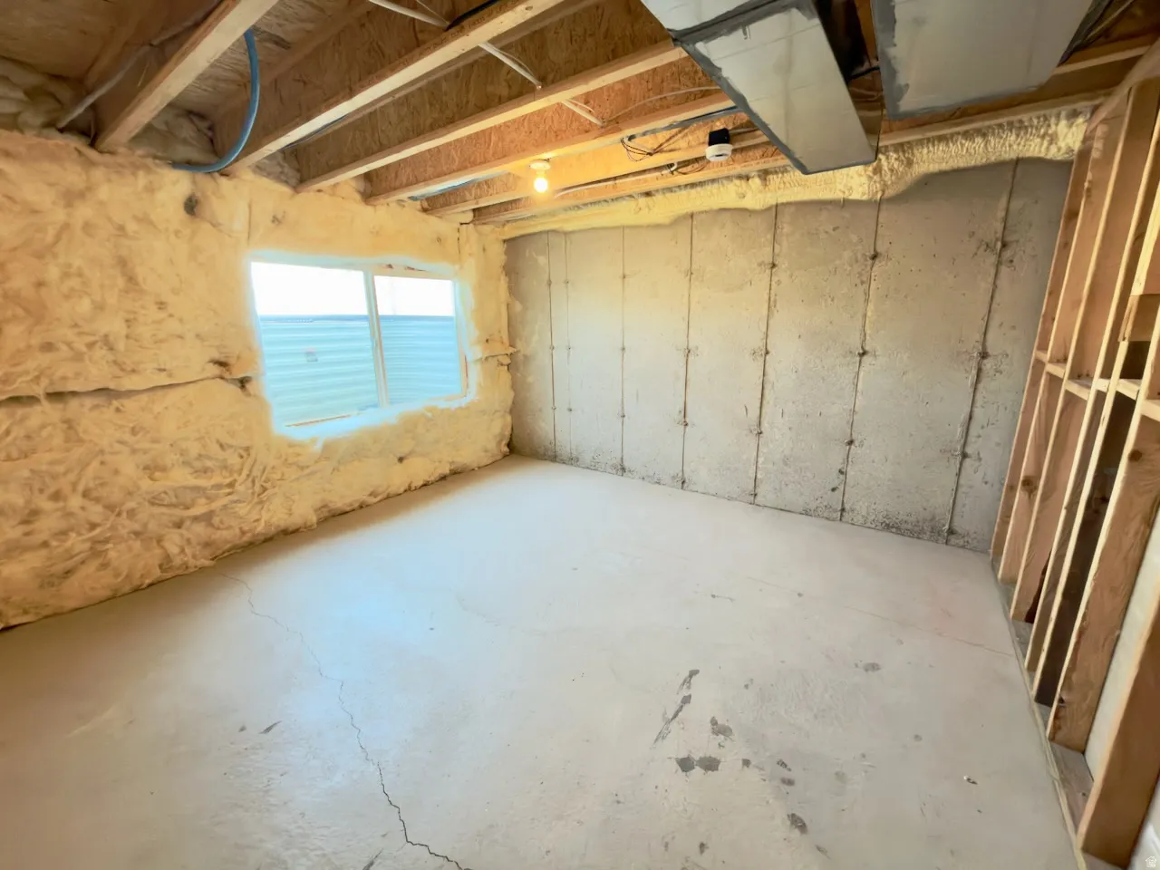 Unfinished basement space featuring exposed ceiling joists, a window opening, and concrete flooring